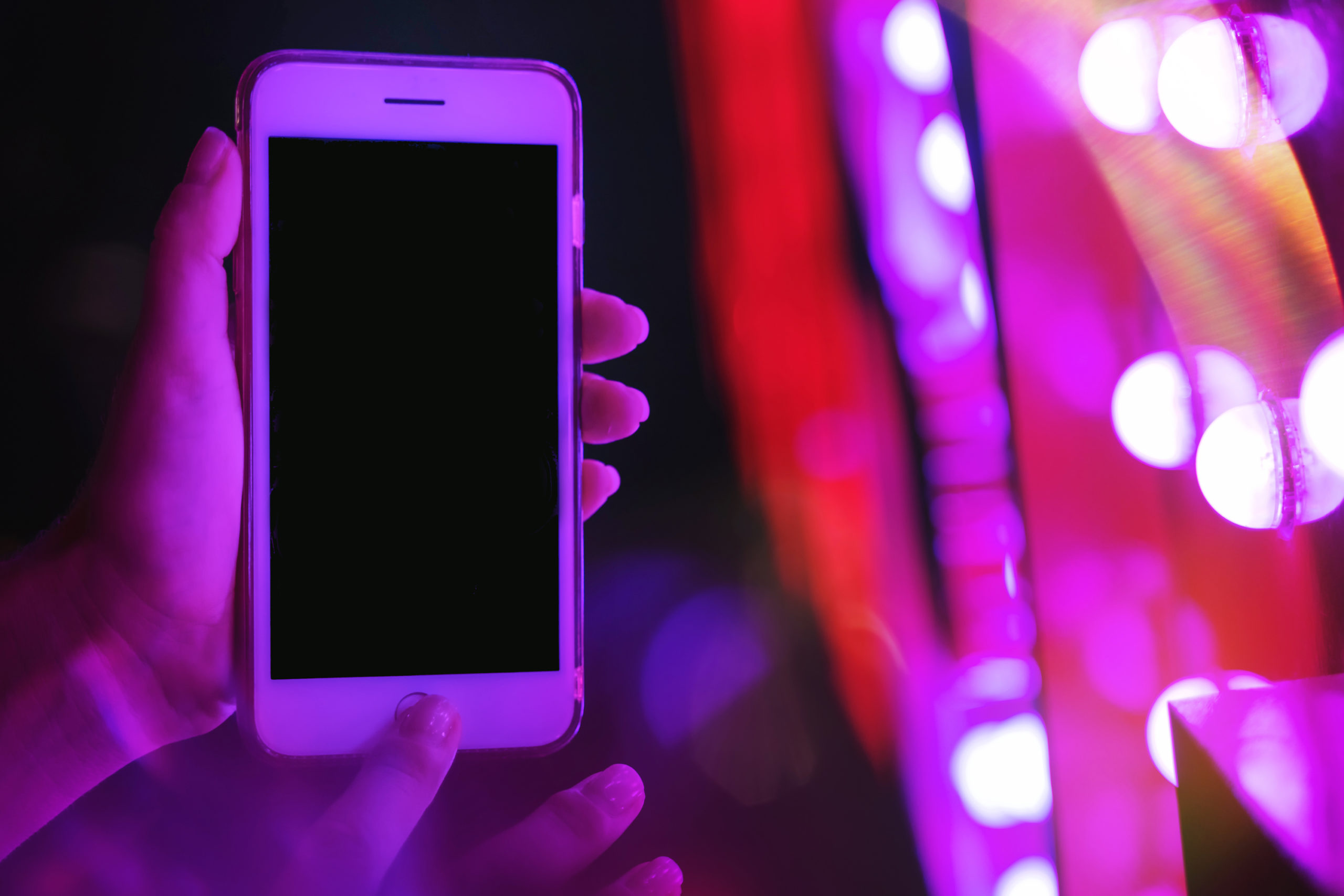 Woman's hand showing smartphone screen in neon blue and pink lights
